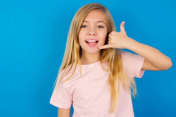 青い壁にピンクのシャツを着た白人の子供は電話のジェスチャーをし 私に電話をかけ 幸せな表情をしています — ストック写真