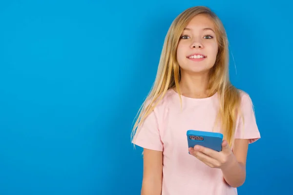 Kavkazská Dívka Růžové Košili Proti Modré Stěně Drží Mobilní Telefon — Stock fotografie