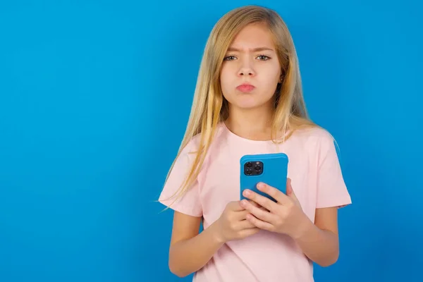 Расстроенная Недовольная Кавказская Девочка Розовой Рубашке Синей Стене Пользуется Мобильным — стоковое фото