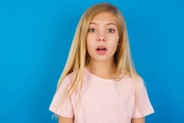 Wstrząśnięty Biały Dzieciak Dziewczyna Różowej Koszuli Przed Niebieską Ścianą Patrzy — Zdjęcie stockowe