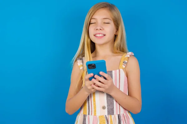 Menina Criança Caucasiana Vestindo Vestido Contra Parede Azul Segurando Gadget — Fotografia de Stock