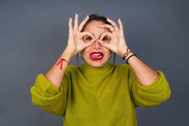 Genç İspanyol kadın dürbün gibi jest yapıyor. Dilini çıkarıyor, gözleri parmaklarından bakıyor. Çılgın ifade.