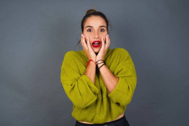 Sersemlemiş genç İspanyol kadın heyecan ve heyecan ifade ediyor, çenesini düşük tutuyor, elleri yanaklarında, gözleri fırlıyor