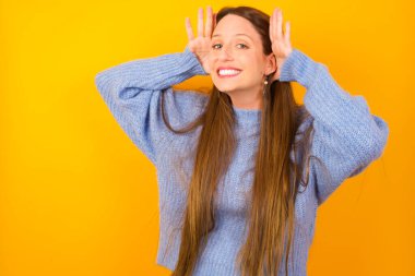 Genç bir kadın iki eliyle kulak hareketi yapmaya çalışıyor. Dedikoduya meraklı. İşitme problemi, sağır