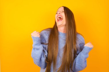 Genç bir kadın şaşkınlıkla ve şaşkınlıkla kollarını kaldırarak ve gözlerini kapatarak başarıyı kutluyor. Kazanan konsept.