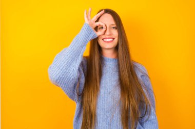 Genç kadın el hareketleriyle gülümsüyor, gözleriyle mutlu yüzüyle parmaklarının arasından bakıyor..
