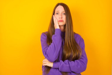 Üzgün, yalnız bir genç kadın yanağına dokunur. El ısırıkları alt dudağını ısırır ve hoşnutsuzca bakar. Kötü duygular