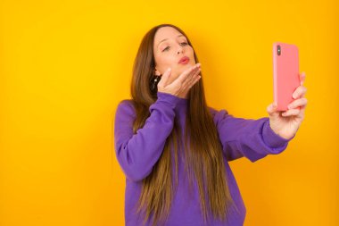 Genç bir kadın akıllı telefon kamerasına hava öpücüğü verip selfie çekiyor ve internetten Mwah 'ı gönderiyor..