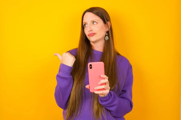 Young Woman Points Thumb Away Shows Blank Space Aside Holds — Stock Photo, Image