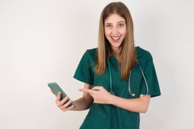 Yeşil gömlekli ve beyaz arka planda steteskobu olan genç ve güzel bir hemşire.