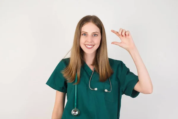 Młoda Kobieta Lekarz Gestykulując Ręką Robi Mały Znak Rozmiaru Palcami — Zdjęcie stockowe