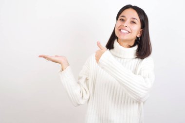 Genç kadın avucunu gösteriyor ve baş parmağıyla iyi bir hareket yapıyor, mutlu ve neşeli gülümsüyor..