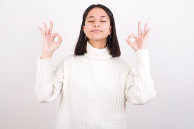 Genç kadın rahatlıyor ve gözleri kapalı gülümsüyor parmaklarıyla meditasyon hareketi yapıyor. Yoga konsepti.