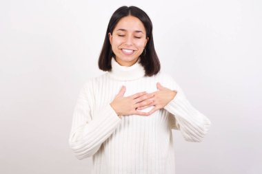 Elleri göğsünde, gözleri kapalı gülümseyen ve yüzünde minnet ifadesi olan genç bir kadın. Sağlık kavramı.