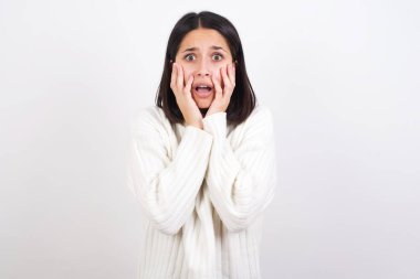 Sersemlemiş genç bir kadın heyecan ve heyecan ifade eder, çenesini indirir, elleri yanaklarında, gözleri fırlar