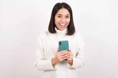 Akıllı telefon tutan heyecanlı genç bir kadın ve iyi haberler aldıktan sonra kameraya hayret içinde bakıyor..