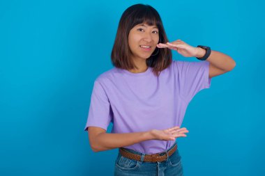 Elleriyle büyük ve büyük bir işaret gösteren, ölçü sembolü olan genç bir kadın. Kameraya bakıp gülümsüyor..