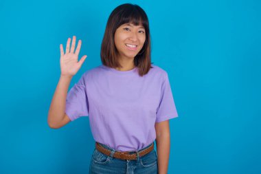 Selam veren genç bir kadın mutlu ve gülümseyen, dostça bir hoş geldin jesti.