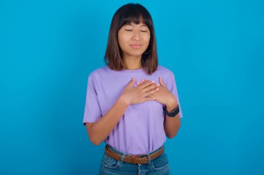 Elleri göğsünde, gözleri kapalı gülümseyen ve yüzünde minnet ifadesi olan genç bir kadın. Sağlık kavramı.