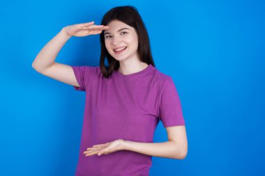 Elleriyle büyük ve büyük bir işaret gösteren, ölçü sembolü olan genç bir kadın. Kameraya bakıp gülümsüyor..