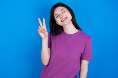 Gülümseyen ve kameraya göz kırpan genç bir kadın zafer işareti yapıyor. İki numara..