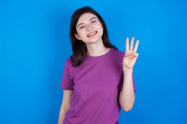 Genç bir kadın kendini beğenmiş ve mutlu bir şekilde gülümserken üç numarayı işaret ediyor..