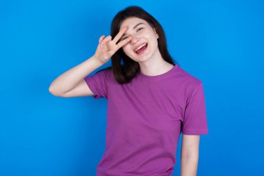 Genç bir kadın barış sembolü yapıyor. Yüzünde parmaklar, gülümseyerek zaferi gösteriyor.