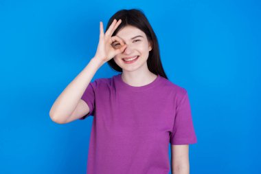 Genç kadın el hareketleriyle gülümsüyor, gözleriyle mutlu yüzüyle parmaklarının arasından bakıyor..