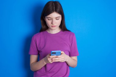 Heyecanlı genç kadın göz kırpıyor, akıllı telefon kullanıyor sosyal ağ haberlerini okuyor.