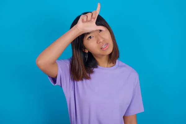 young woman  making fun of people with fingers on forehead doing loser gesture mocking and insulting.
