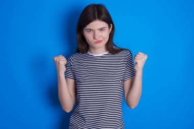 Öfkeli genç bir kadın, öfkeyle yanaklarına vurur ve yumruklarını kaldırır. Öfke ve agresif duyguları ifade eder. Öfkeli model