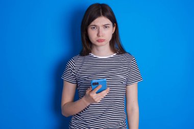 Memnun olmayan genç bir kadın mobil yazılım uygulaması kullanıyor ve internette bilgi sörfü yapıyor.