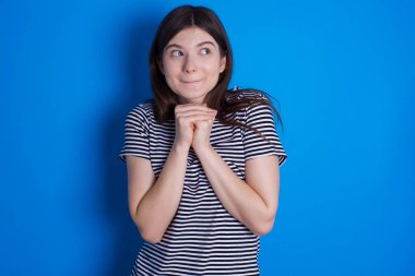 Meraklı genç bir kadın ellerini çenesinin altında tutar dudaklarını ısırır ve ilgilenir..