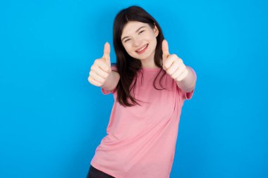 Genç, esmer bir kadın elleriyle olumlu bir jest yapmayı onaylıyor. Gülümsüyor ve başarı için seviniyor. Kazanan jest.