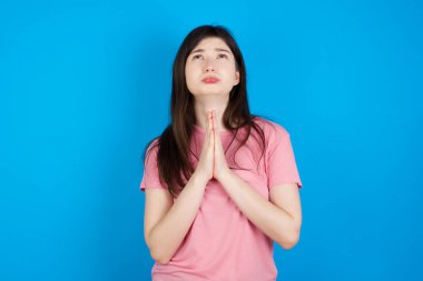 Genç esmer kadın elleri bağlı yalvarıyor ve dua ediyor. Yüzünde umut ifadesi var. Çok duygusal ve endişeli. Lütfen Tanrım.