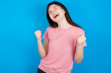 Genç esmer kadın şaşkınlık ve şaşkınlık içinde kollarını kaldırarak ve gözlerini kapatarak başarıyı kutluyor. Kazanan konsept.