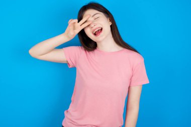 Genç esmer kadın barış sembolü yapıyor. Yüzünde parmaklar, gülümseyerek zaferi gösteriyor.