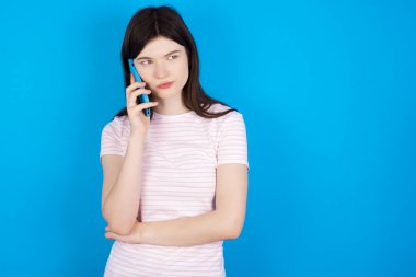 Sad young brunette woman talking on smartphone. Communication concept.