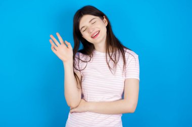 Overjoyed successful young brunette woman raises palm and closes eyes in joy being entertained by friends