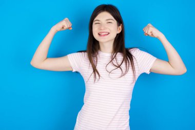 Strong powerful young brunette woman toothy smile, raises arms and shows biceps. Look at my muscles!