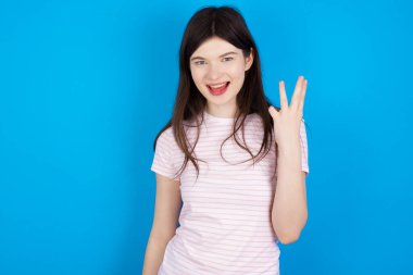 young brunette woman smiling and looking friendly, showing number three or third with hand forward, counting down