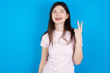 young brunette woman smiling and looking friendly, showing number two or second with hand forward, counting down