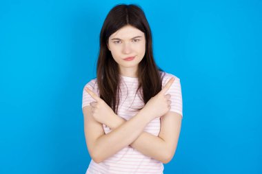 Serious young brunette woman crosses hands and points at different sides hesitates between two items. Hard decision concept