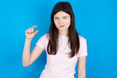 Displeased young brunette woman shapes little hand sign demonstrates something not very big. Body language concept.