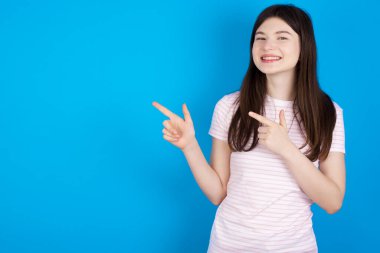 Optimistic young brunette woman points with both hands and  looking at empty space.