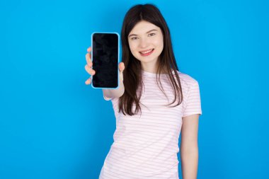 Charming adorable young brunette woman holding modern device, showing black screen smartphone