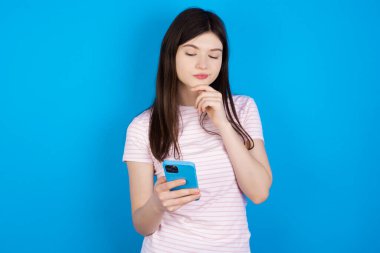 Düşünceli, mutlu, esmer kadın telefona, kopyasına bakıyor.