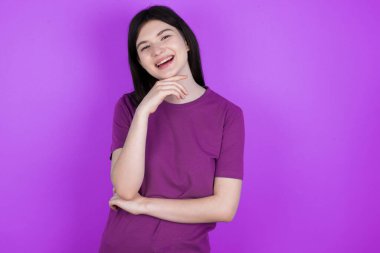 İyimser genç esmer kadın ellerini kısmen çapraz tutuyor ve elleri çenesinin altında, zevkle kameraya bakıyor. Mutlu duygu konsepti.