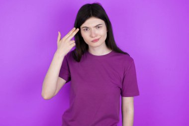 Mutsuz genç esmer kadın intihar jesti yapıyor ve tabancayı eliyle taklit ediyor, dudaklarını kıvırıyor, iki parmağını da tapınakta tutuyor.