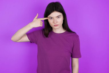 Mutsuz genç esmer kadın intihar jesti yapıyor ve tabancayı eliyle taklit ediyor, kıvrımlı dudaklar iki parmağını şakakta tutuyor, ateş ediyor, her şeyden bıkıyor.,